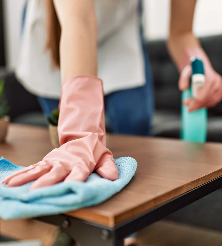 Person wischt einen Couchtisch mit einem Tuch und Reinigungsmittel.