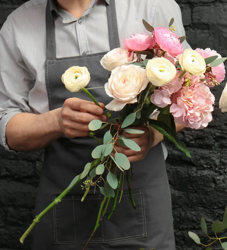 Person bindet einen Blumenstrauß aus Rosen und Blüten.