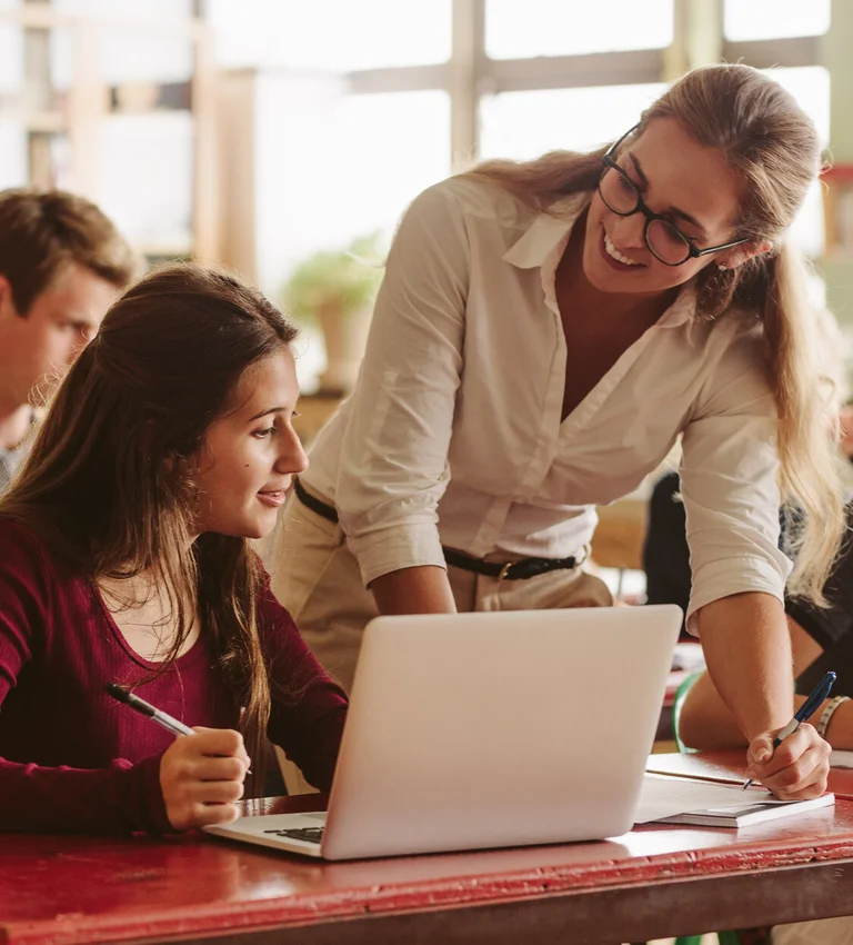 Lehrkraft unterstützt Schülerinnen und Schüler bei der Arbeit am Laptop im Klassenraum.