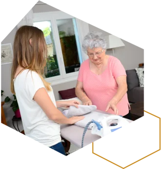 Pflegekraft misst einer älteren Frau im Wohnzimmer den Blutdruck.