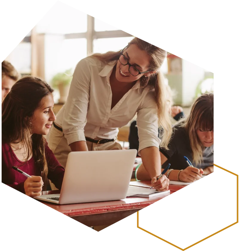 Lehrkraft unterstützt Schülerinnen und Schüler bei der Arbeit am Laptop im Klassenraum.