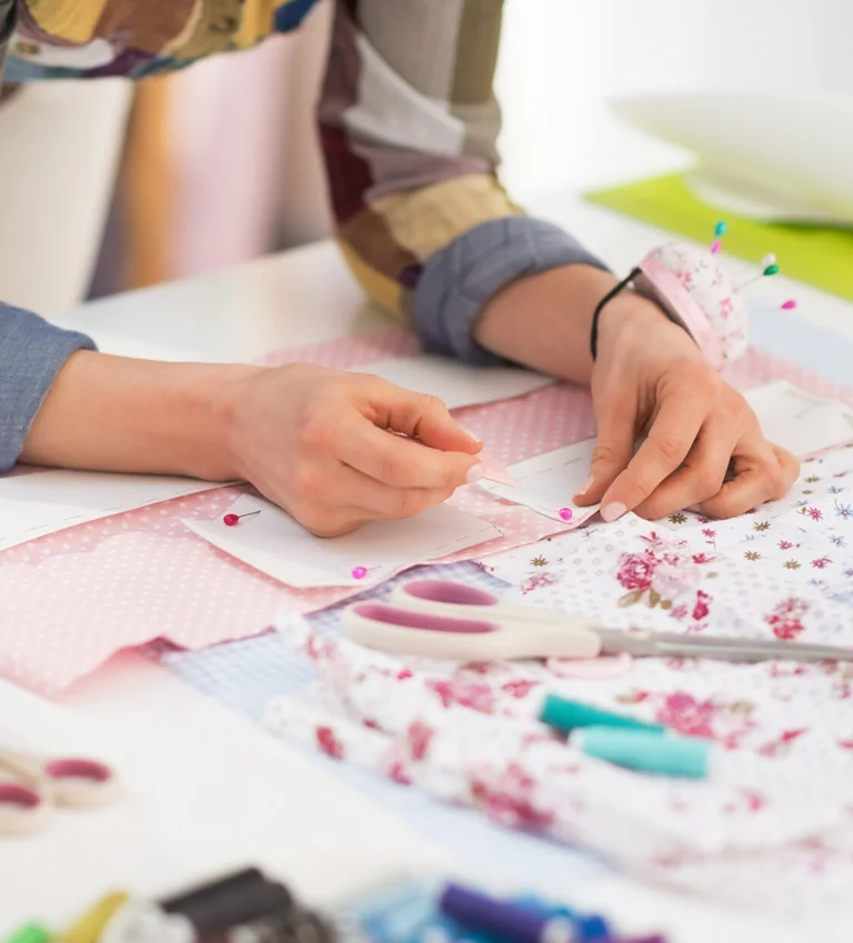 „Person arbeitet an einem Nähprojekt mit Stoff und Schnittmuster auf dem Tisch.