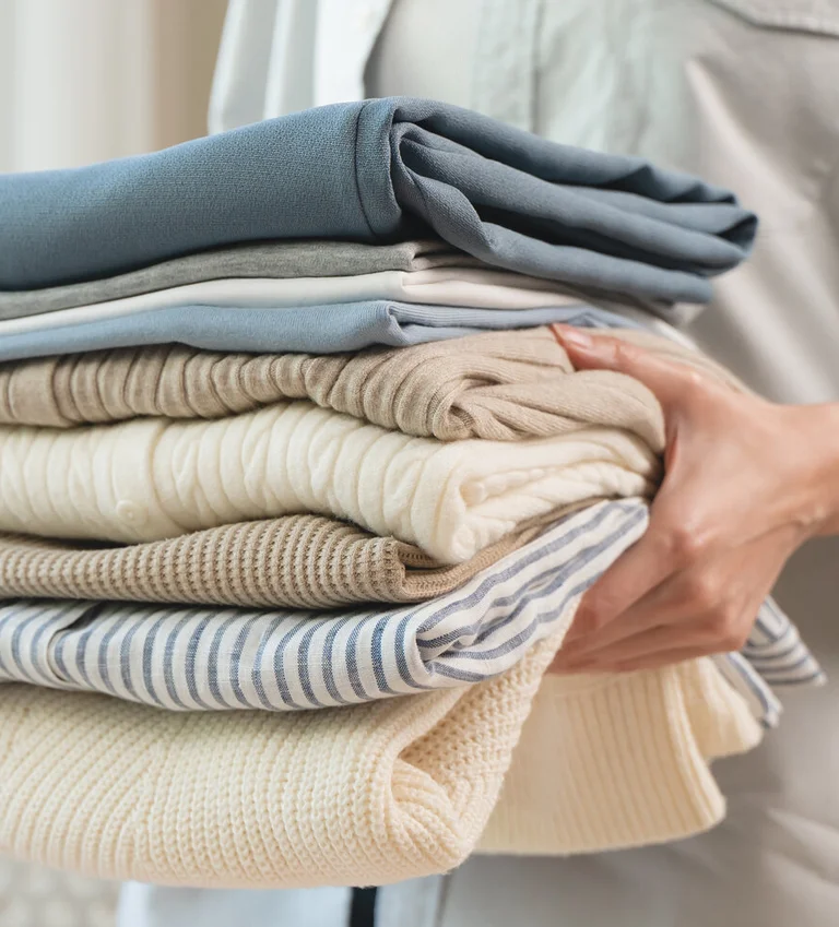 Hände halten einen Stapel frisch gefalteter Wäsche.