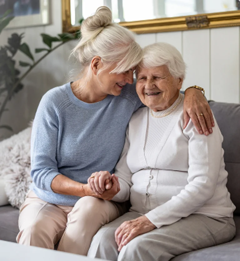 Zwei ältere Frauen sitzen auf dem Sofa und halten sich an den Händen