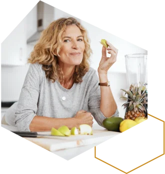 Frau isst einen Apfel in der Küche; Obst liegt auf dem Tisch.