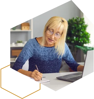 Frau schreibt Notizen am Schreibtisch neben einem Laptop.